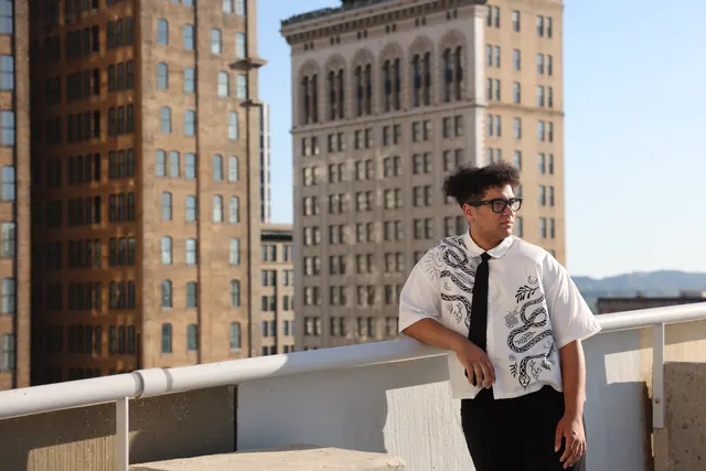 Will Smith leaning on a rooftop railing with downtown buildings behind him